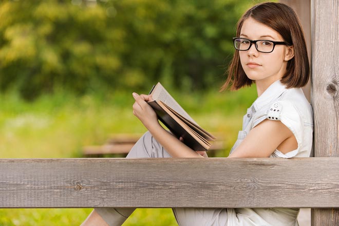 Bambina che legge un libro all'aperto.